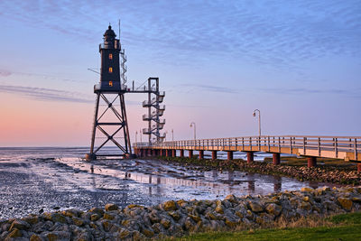 Lighthouse by sea against sky during sunset