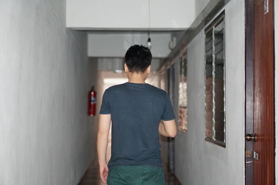 Rear view of man standing against wall at home