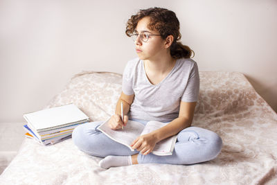 Young woman looking away while sitting on bed