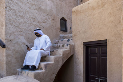 Man wearing traditional clothing using smart phone while sitting on steps