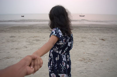 Woman with arms raised on beach against sky