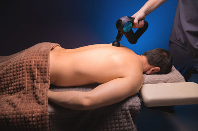 Physiotherapy of the upper back with a percussion massager. therapist kneads the patient's upper