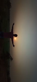 Silhouette man in water against sky during sunset