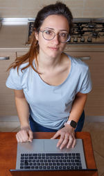 Young women in light blue t-shirt using laptop in the kitchen at home 