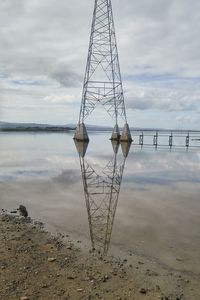 Electricity pylon on beach against sky