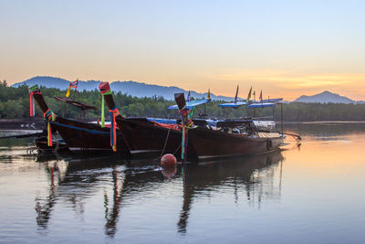 Fishing boats moored in sea against sky during sunset