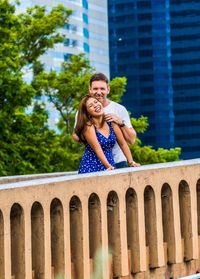 Portrait of happy couple standing on footbridge in city