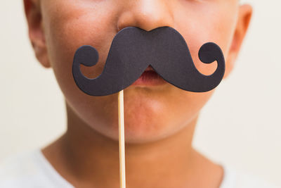 Midsection of boy holding mustache prop over lips