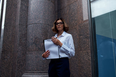 Woman holding umbrella while standing against wall