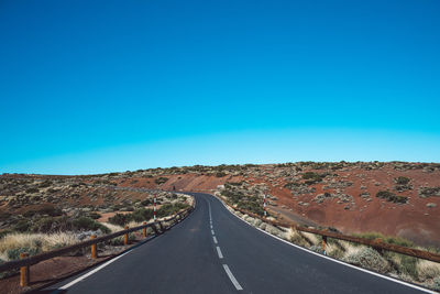 Empty road along landscape against clear blue sky