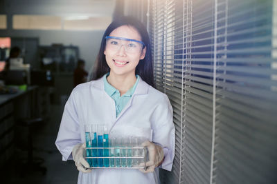 Portrait of female scientist holding test tube while standing at laboratory