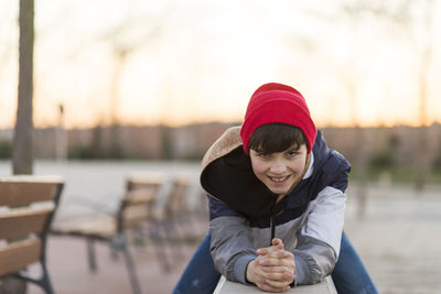 Portrait of boy sitting on retaining wall against sky during sunset