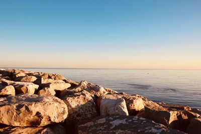 Rocks by sea against clear blue sky