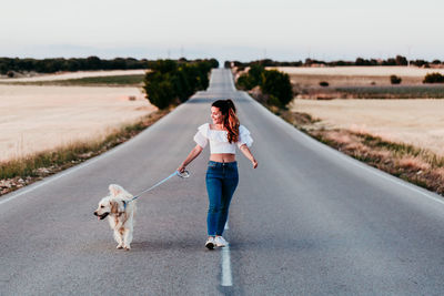 Woman walking with dog on road amidst field