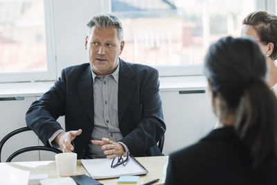 Mature businessman sitting and explaining coworkers at office