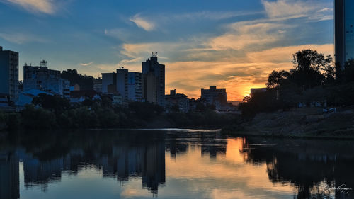 Scenic view of lake by buildings against sky during sunset