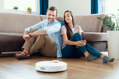 Portrait of smiling friends using mobile phone while sitting on sofa at home