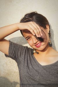 Portrait of smiling young woman shielding eyes against wall