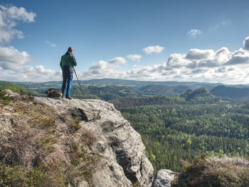 Man standing on rock looking at mountains against sky