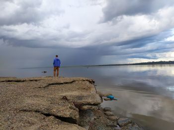 Rear view of man standing on rock against sky