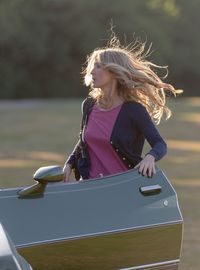 Woman looking away while standing by vehicle door