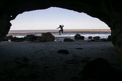 Silhouette people on rocks at beach against sky