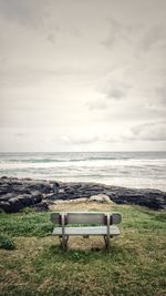 Empty bench on shore by sea against sky