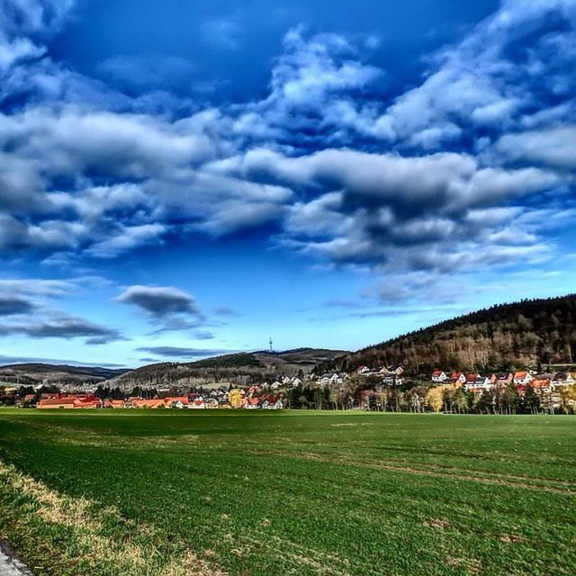 sky, building exterior, landscape, architecture, built structure, cloud - sky, field, house, grass, cloud, scenics, beauty in nature, tranquil scene, nature, rural scene, village, tree, residential structure, mountain, cloudy