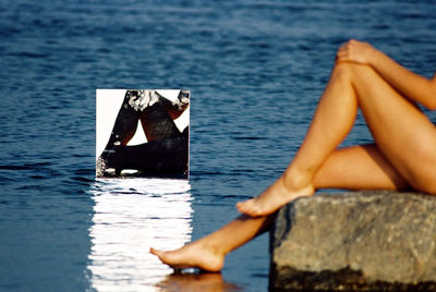 Low section of woman sitting on rock by sea reflecting in mirror