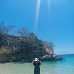 Rear view of woman standing by sea against blue sky