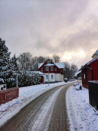 Snow covered road by building against sky during winter