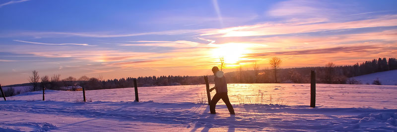 Man standing on snow covered field against sky during sunset