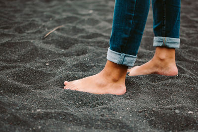 Anonymous barefoot female in jeans standing on black volcanic soil on beach of la palma island in spain