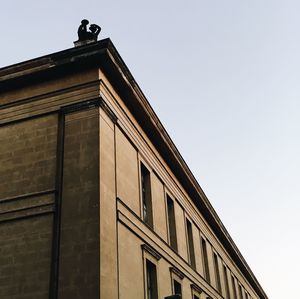 Low angle view of bird perching on building against clear sky