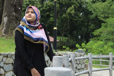 Thoughtful teenage girl in hijab standing against trees
