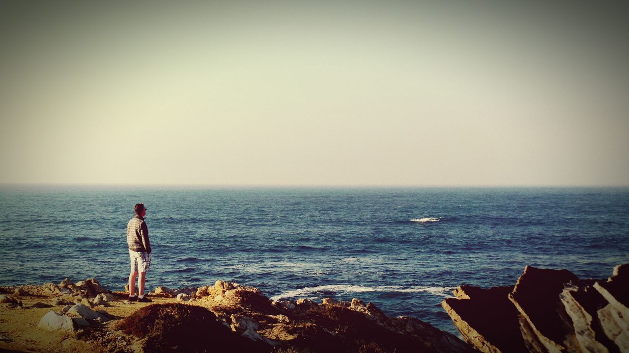 sea, horizon over water, water, standing, lifestyles, leisure activity, full length, rear view, scenics, copy space, tranquility, tranquil scene, beauty in nature, clear sky, shore, rock - object, nature, men