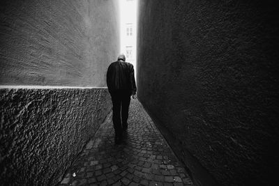Rear view of woman walking on footpath against wall