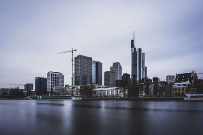 Modern buildings by river against sky in city