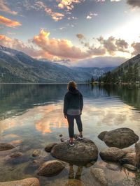 Rear view of woman standing on rock by lake against sky