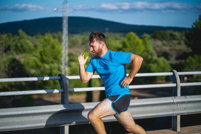 Young man jogging on by railing against sky