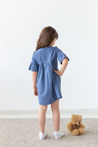 Rear view of girl with toy standing against wall