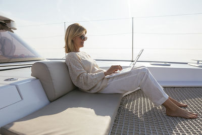 Woman sitting on catamaran, using laptop