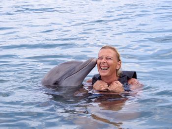 High angle view of cheerful woman swimming with dolphin in sea