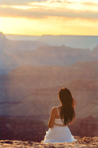 Rear view of woman sitting on mountain during sunset