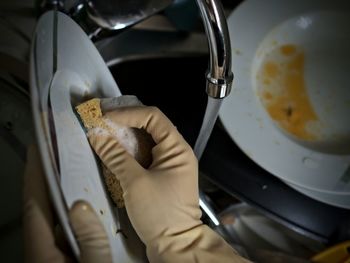 Close-up of gloved hands washing plate with sponge