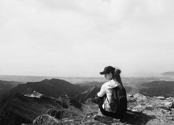Side view of woman sitting on mountain against sky