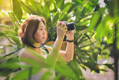 Portrait of young woman photographing through smart phone outdoors