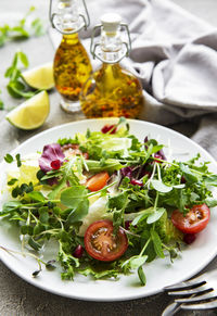 Fresh green mixed salad bowl with tomatoes and microgreens on concrete background. 
