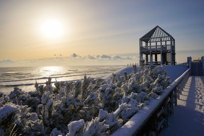 Panoramic shot of snow covered land and sea against sky during sunset
