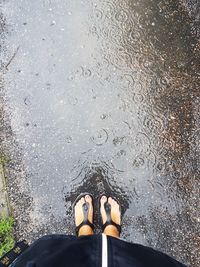 Low section of woman standing near puddle on road during monsoon